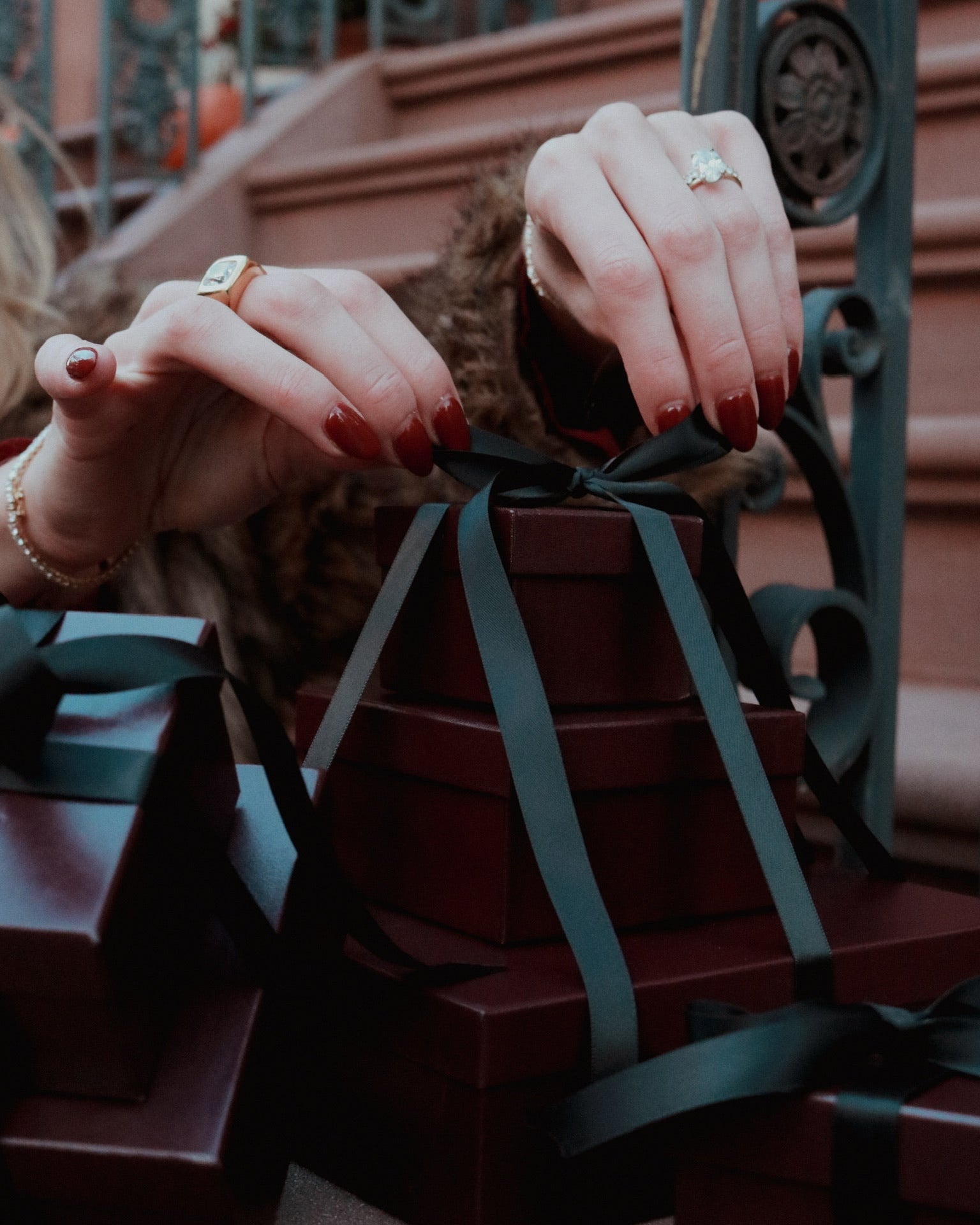 Close-up of hands holding a gift box with ribbons against an iron railing background
