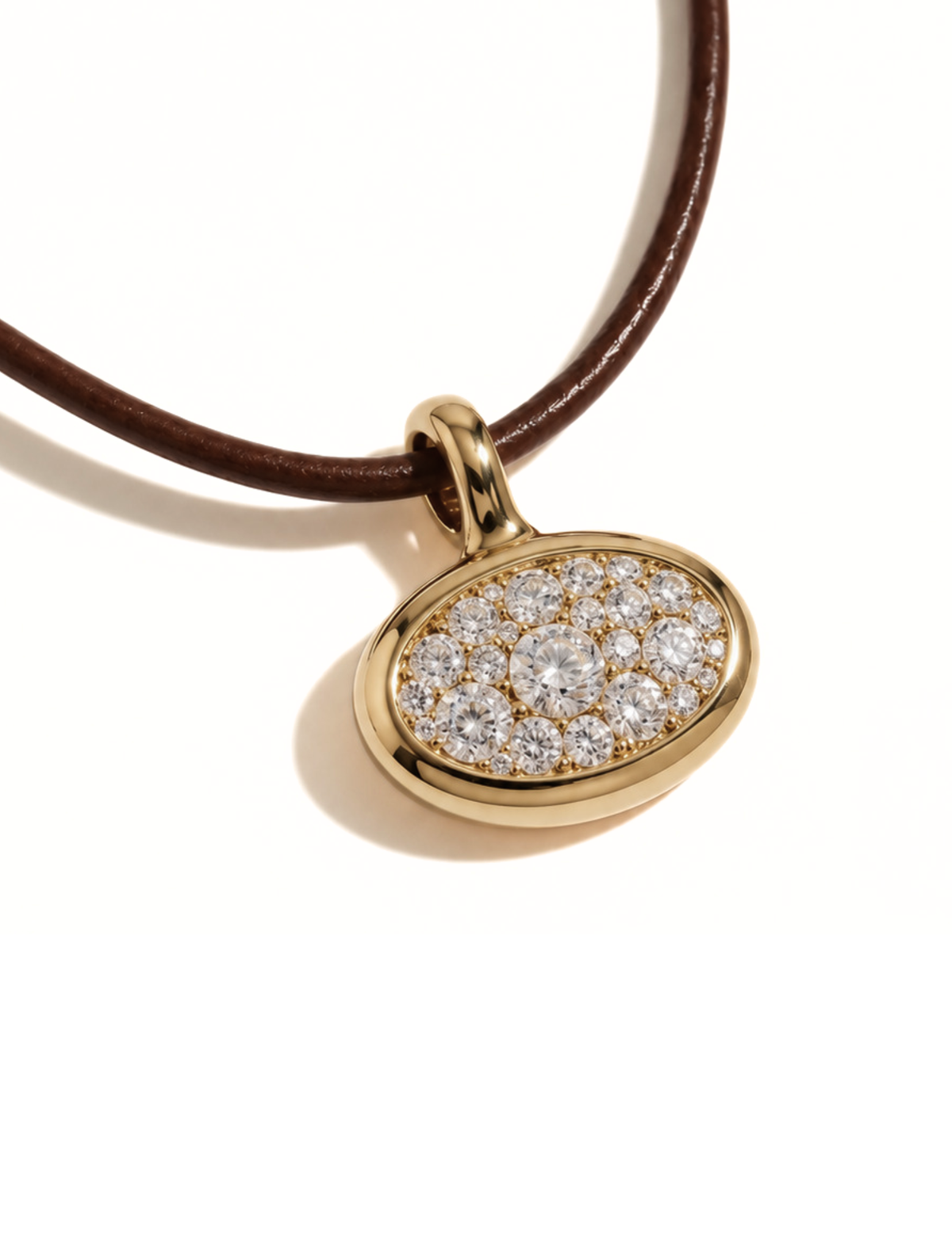 An oval pendant necklace featuring a pavé diamond center set in a gold frame, suspended from a dark brown leather cord, shown on a clean white background.