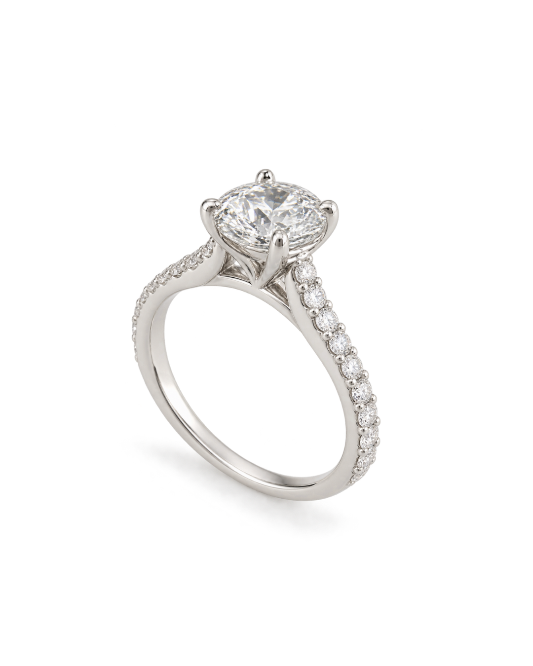 A silver-toned solitaire engagement ring featuring a round-cut center stone and a pavé-set band with small accent stones, shown on a clean white background.
