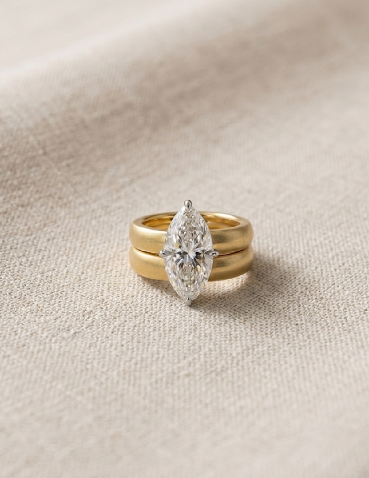 Gold ring with a pear-shaped diamond on a beige fabric background